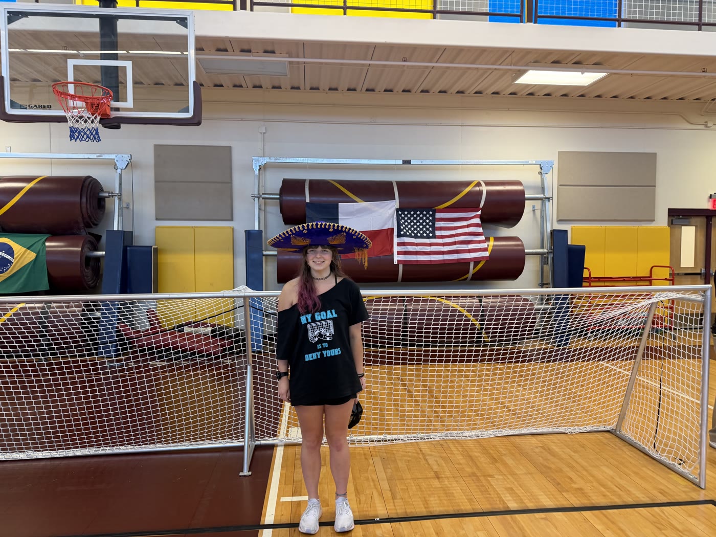 Tayler smiling at the goal during a team event, wearing a My Goal Is To Be Out There shirt.